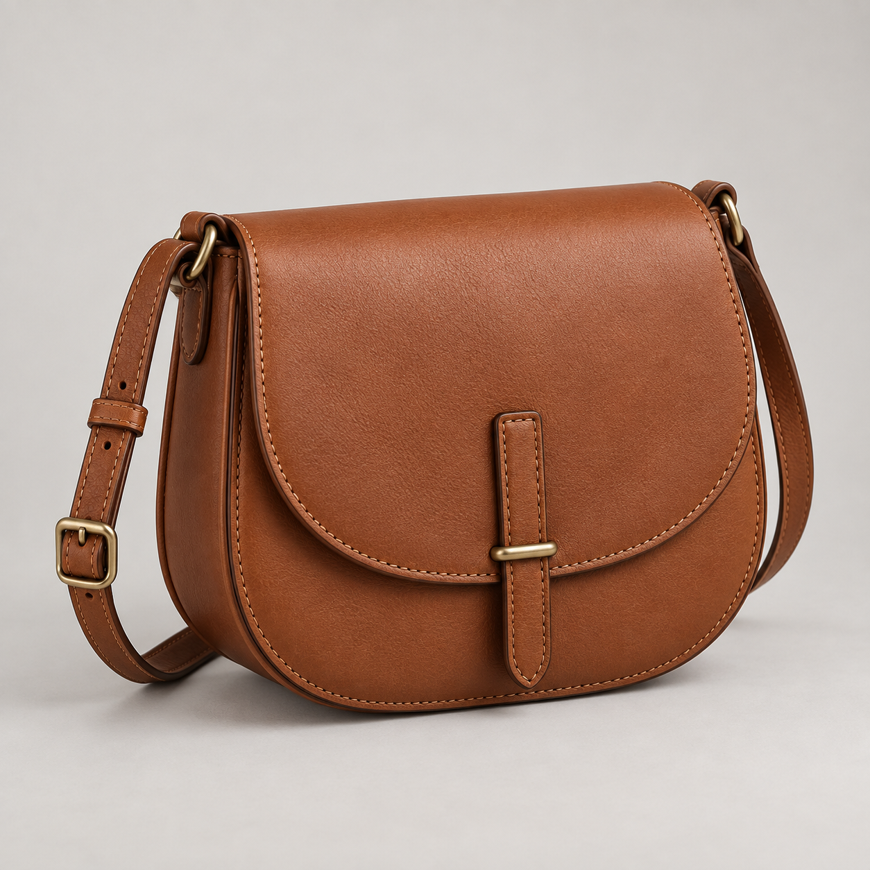 Cognac Saddle: Curved saddle silhouette with a rounded front flap and a slender adjustable strap. Illustrative design reference.